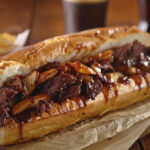 Authentic Philly cheesesteak sandwich with ribeye beef, melted provolone cheese, caramelized onions, and a toasted Amoroso hoagie roll served with crispy fries and iced tea.